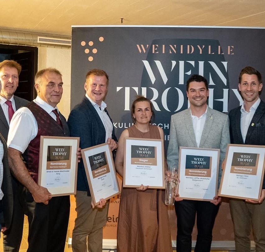 Fünf Personen, die Trophäen mit Urkunden halten, stehen vor einem großen Banner mit dem Text Weintrophy 2023.