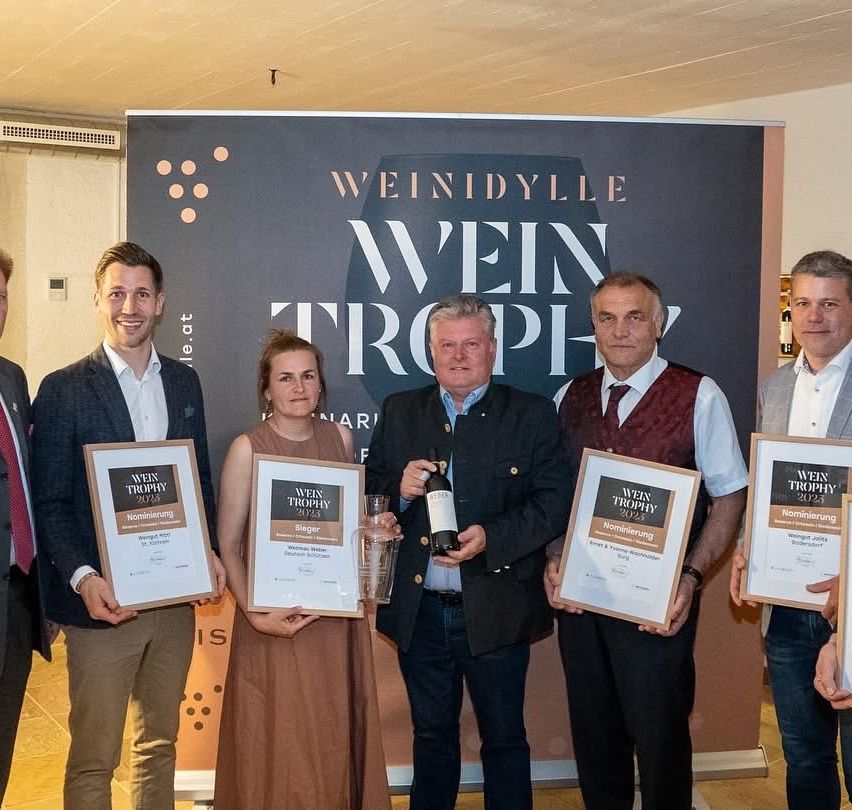 Fünf Personen stehen nebeneinander vor einem Banner. Sie halten Auszeichnungen und Flaschen.