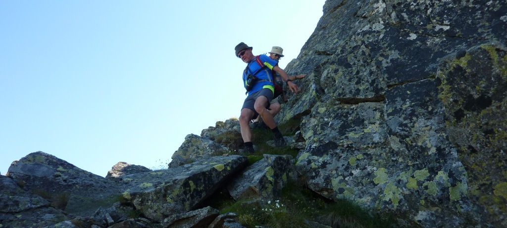 Zwei Männer erklimmen einen steilen felsigen Berg, einer trägt einen Hut und der andere eine Sonnenbrille.