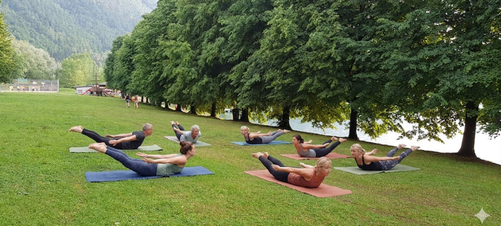 Eine Gruppe von Menschen macht Yoga in einem Grasbereich in der Nähe eines Gewässers.