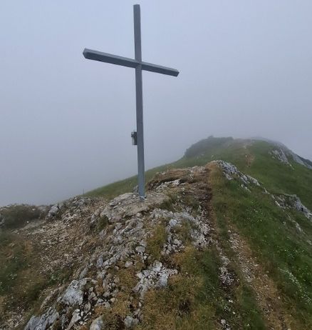 Ein Metallkreuz steht auf einem felsigen Hügel unter einem nebligen Himmel.