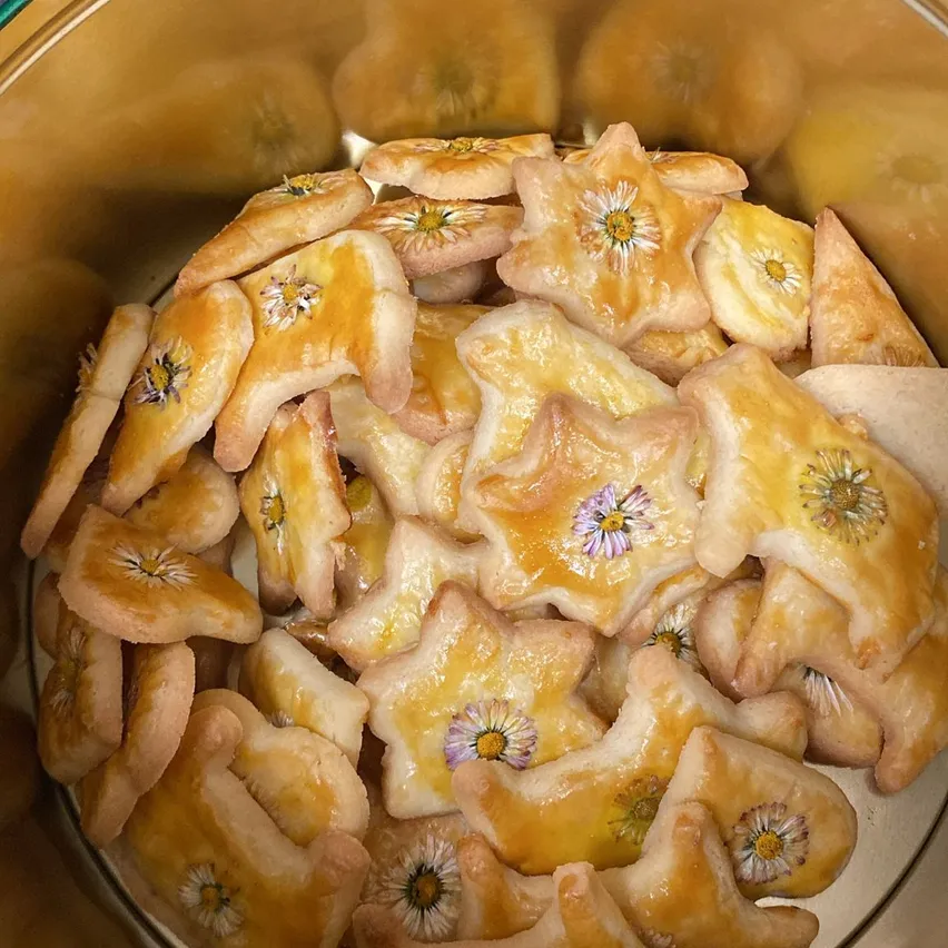 Eine Schüssel voller sternförmiger Kekse, jeder mit einer Blume gekrönt. Die Kekse haben eine goldbraune Kruste und sind in der Schüssel verstreut.