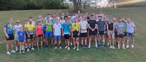 Eine Gruppe von Menschen in Sportbekleidung, die in einer Reihe auf einem Rasenfeld stehen, mit Bäumen im Hintergrund.