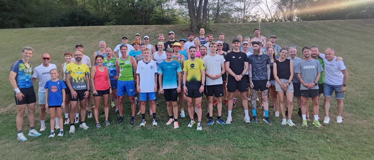 Eine Gruppe von Menschen in Sportbekleidung, die in einer Reihe auf einem Rasenfeld stehen, mit Bäumen im Hintergrund.