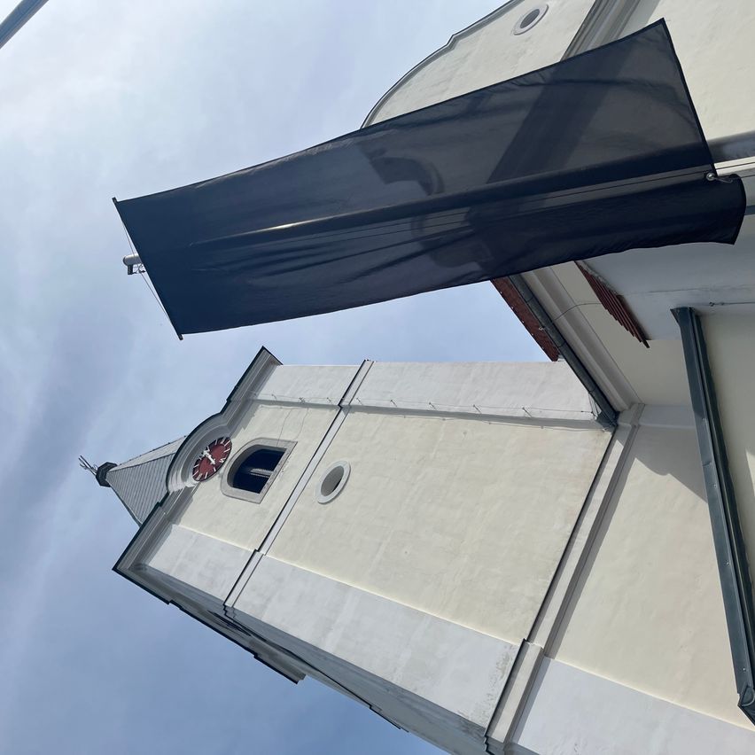 Ein Blick auf den Turm einer Kirche mit einer Uhr und einem schwarzen Tuch, das daran hängt.