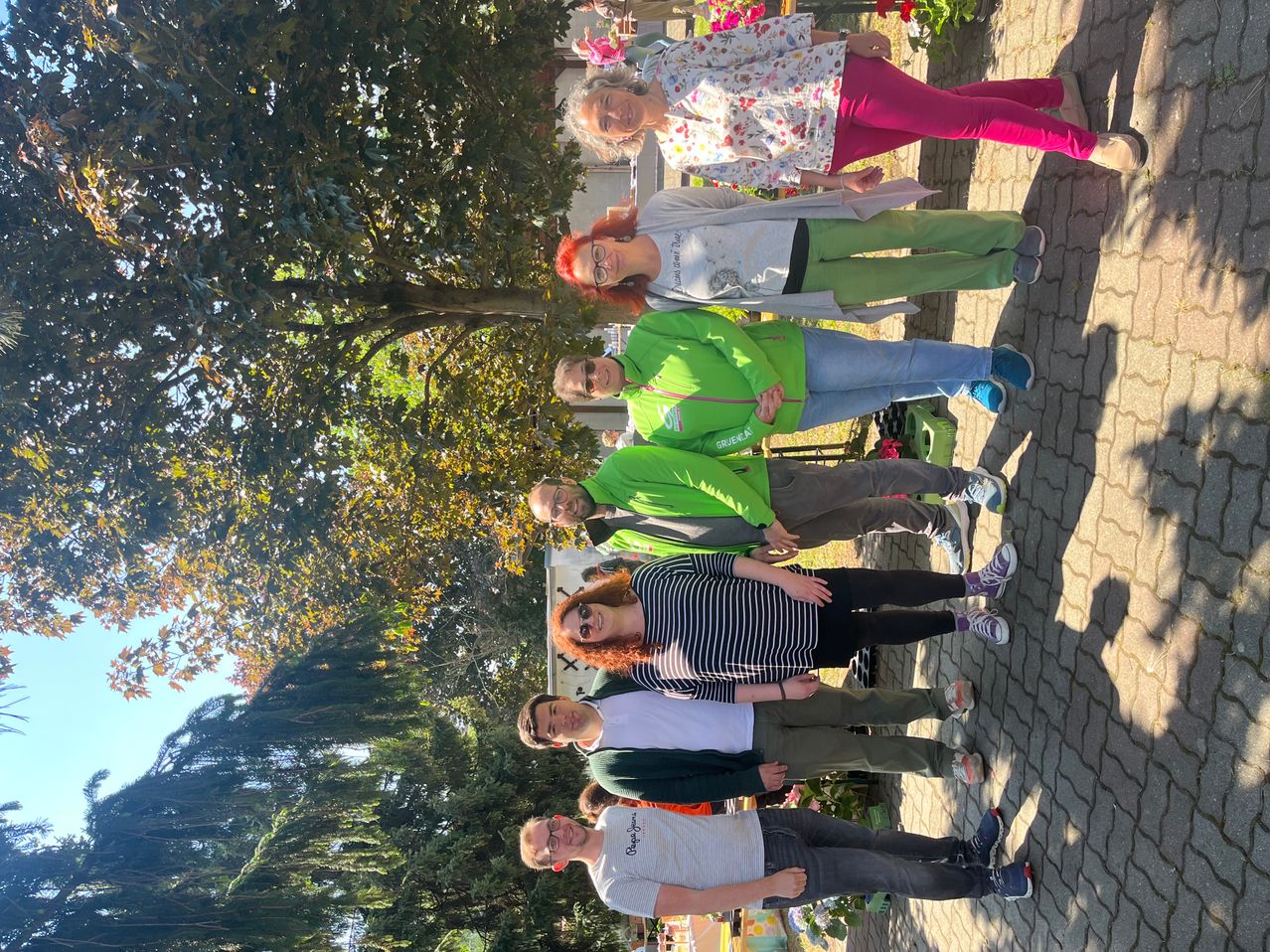 Eine Gruppe von Menschen in grünen und weißen Shirts posiert für ein Foto auf einem Ziegelweg, umgeben von Bäumen.