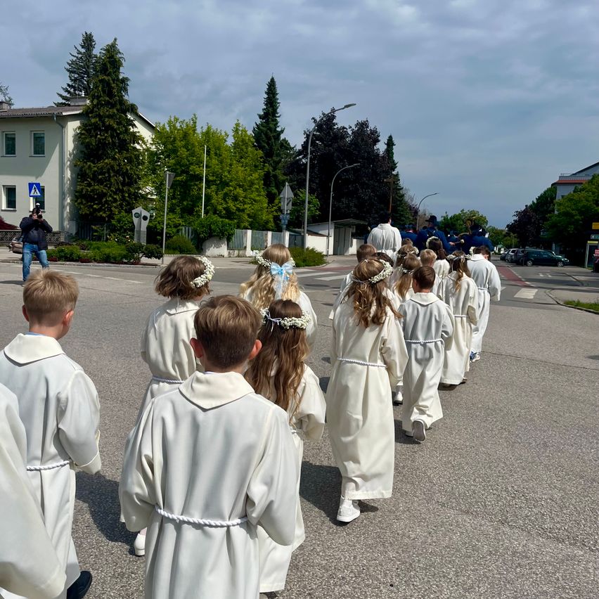 Eine Gruppe von Kindern in weißen Gewändern geht die Straße entlang, wahrscheinlich für eine religiöse Veranstaltung, während ein Fotograf den Moment festhält.