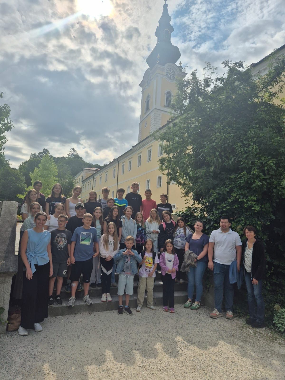 A group of children and adults pose for a photo in front of a yellow building with a tower.