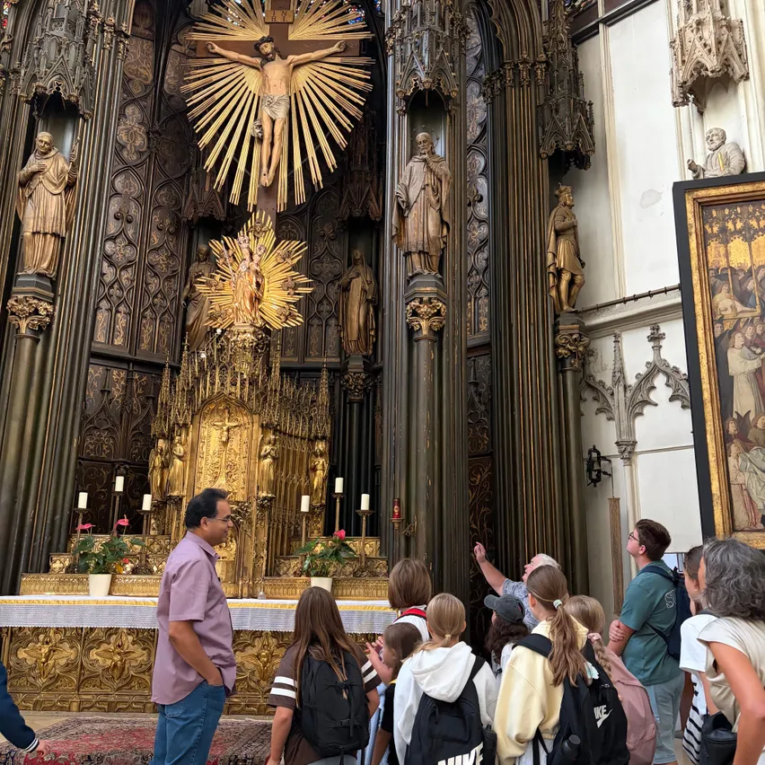 Eine Gruppe von Menschen steht vor einem goldenen Altar in einer Kirche, mit einem großen Kruzifix und Statuen dahinter.