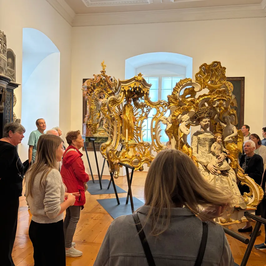 Besucher in einem Museum bewundern komplizierte goldene Skulpturen, eine zeigt eine sitzende Frau mit einem Kind.