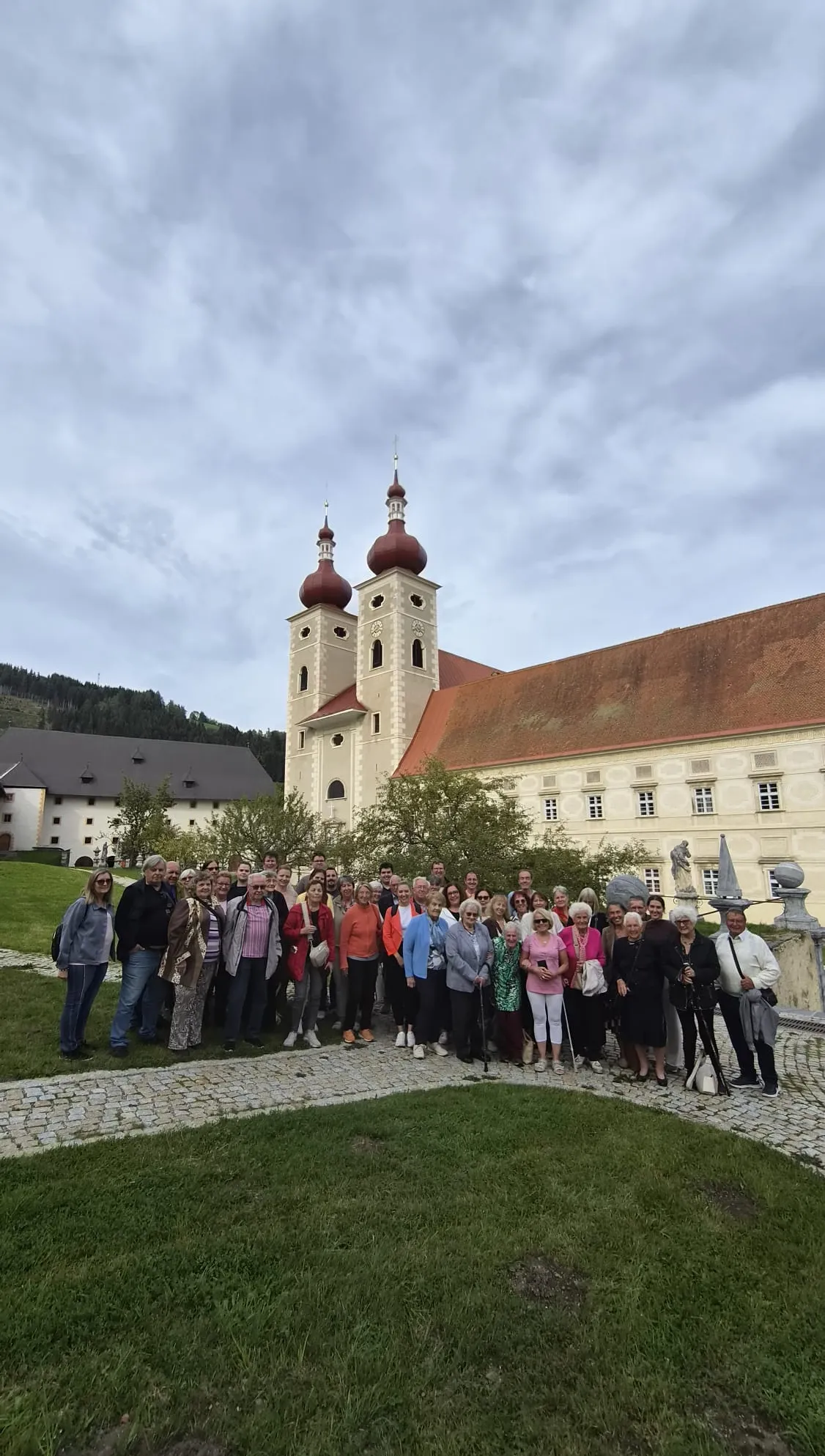Eine Gruppe von Menschen posiert für ein Foto vor einer historischen Kirche mit roten Kuppeln und einem roten Dach.