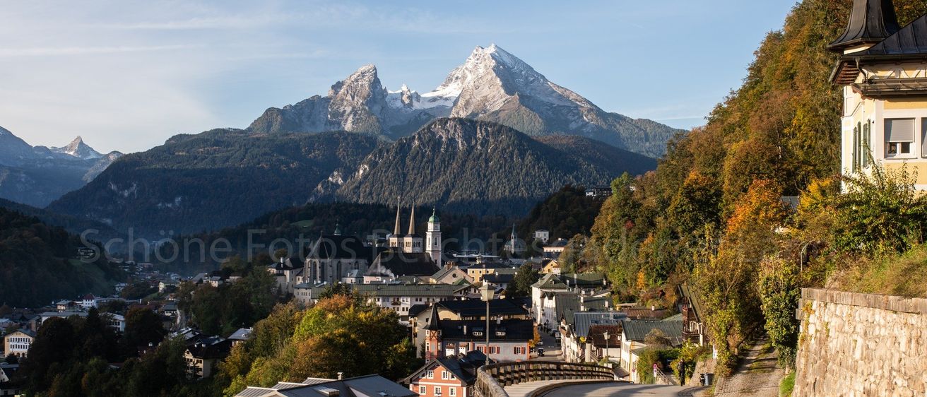 Ein malerisches Dorf am Fuße schneebedeckter Berge. Das Dorf besteht aus einer Mischung aus traditionellen und modernen Gebäuden, mit einer kurvenreichen Straße, die den Hügel hinaufführt.