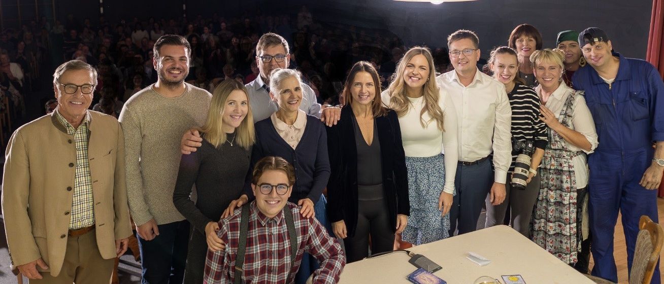 Eine Gruppe von Menschen, einschließlich Erwachsener und Kinder, posiert für ein Foto in einem Innenbereich mit Holzbalken, einem Basketballkorb und einem Tisch mit Karten.