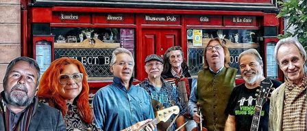 Sechs Musiker stehen vor einem roten Gebäude, möglicherweise einer Bar, namens Sean Tierney. Die Musiker halten verschiedene Instrumente, darunter ein Akkordeon, eine Geige und eine Gitarre.