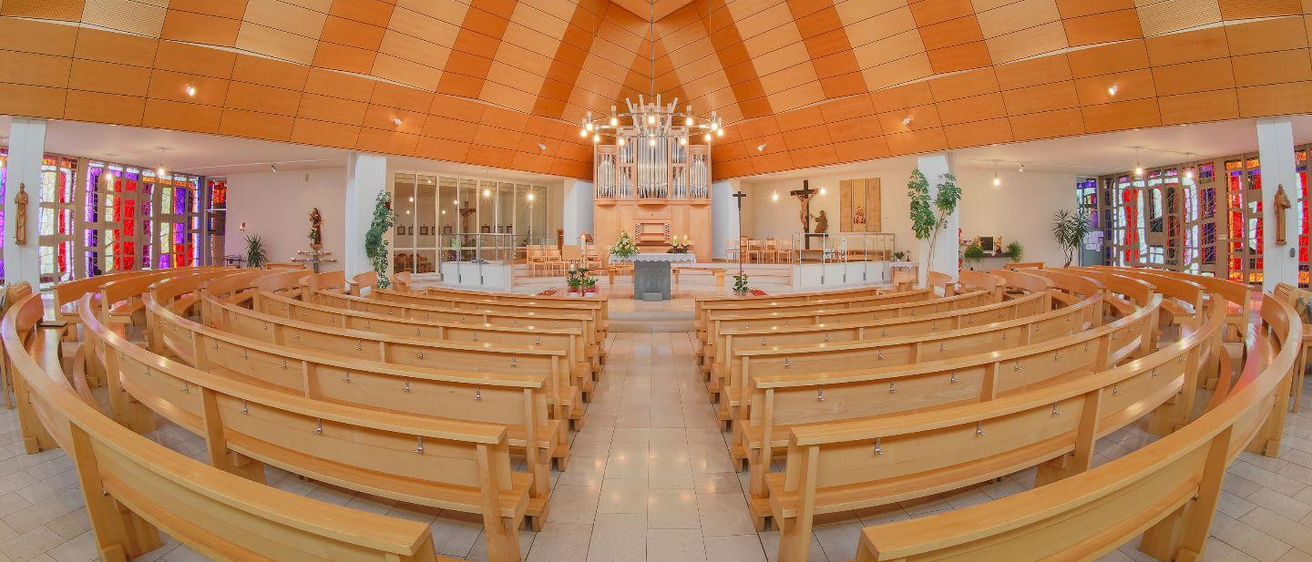 Eine leere Kirche mit hölzernen Kirchenbänken, einem Kreuz, einer Kanzel und einer Orgel unter einer orange gestreiften Decke.