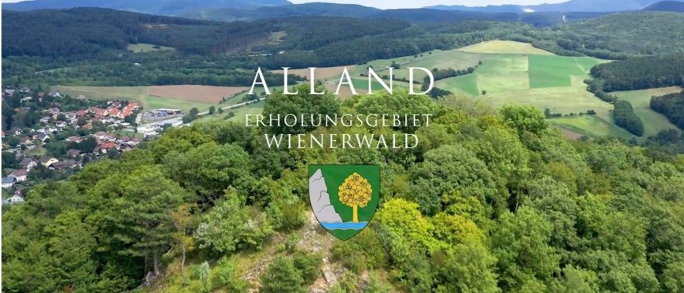 An aerial view of Alland, a recreational area with lush green trees, mountains, and a village below. The image features the region's logo.