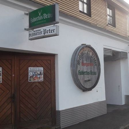 Ein deutsches Pub mit einer Holztür und einem Fassschild, auf dem 'Fubtertus Brau' steht. Das Schild über der Tür zeigt 'Schwarzer Peter'.