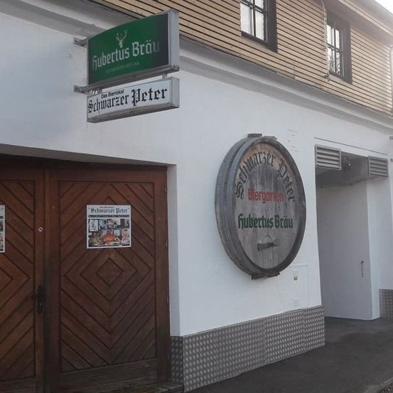 Ein deutsches Pub mit einer Holztür und einem Fassschild, auf dem 'Fubtertus Brau' steht. Das Schild über der Tür zeigt 'Schwarzer Peter'.
