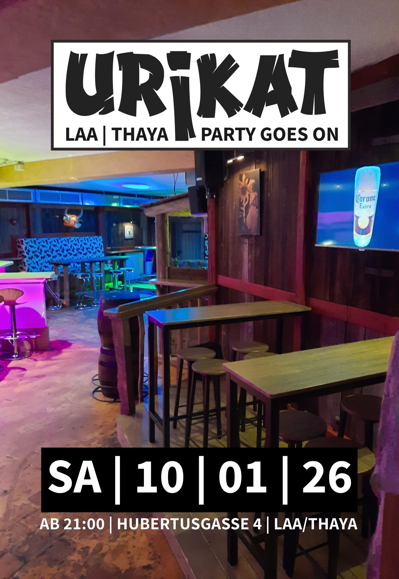 Ein lebhaftes Bar-Interieur mit Holztischen, Stühlen und einem Monitor, der eine Corona Extra Flasche zeigt. Die Bar hat eine Holzwand und lila Beleuchtung. Es gibt ein Schild, das 'LAA | THAYA PARTY GOES ON' steht.