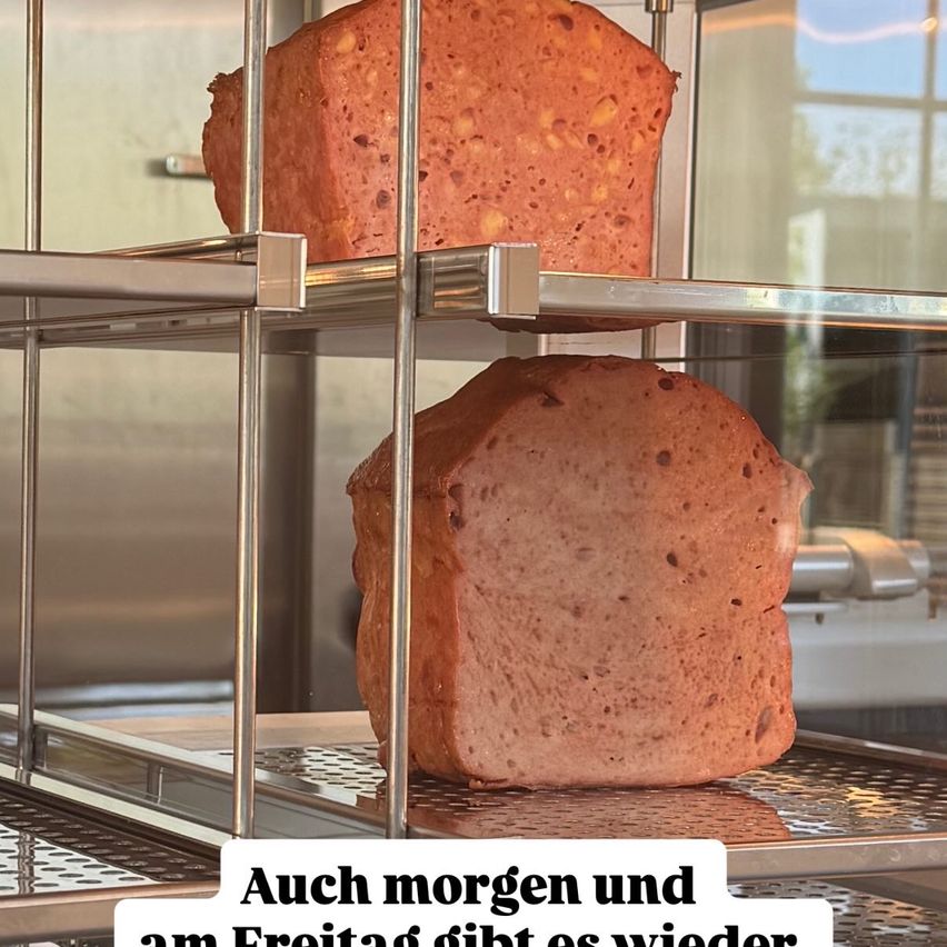 Zwei Brotlaibe sind auf einem Metallregal gestapelt. Der obere hat eine leicht angebrannte Kruste. Der untere ist goldbraun. Beide sehen frisch aus.