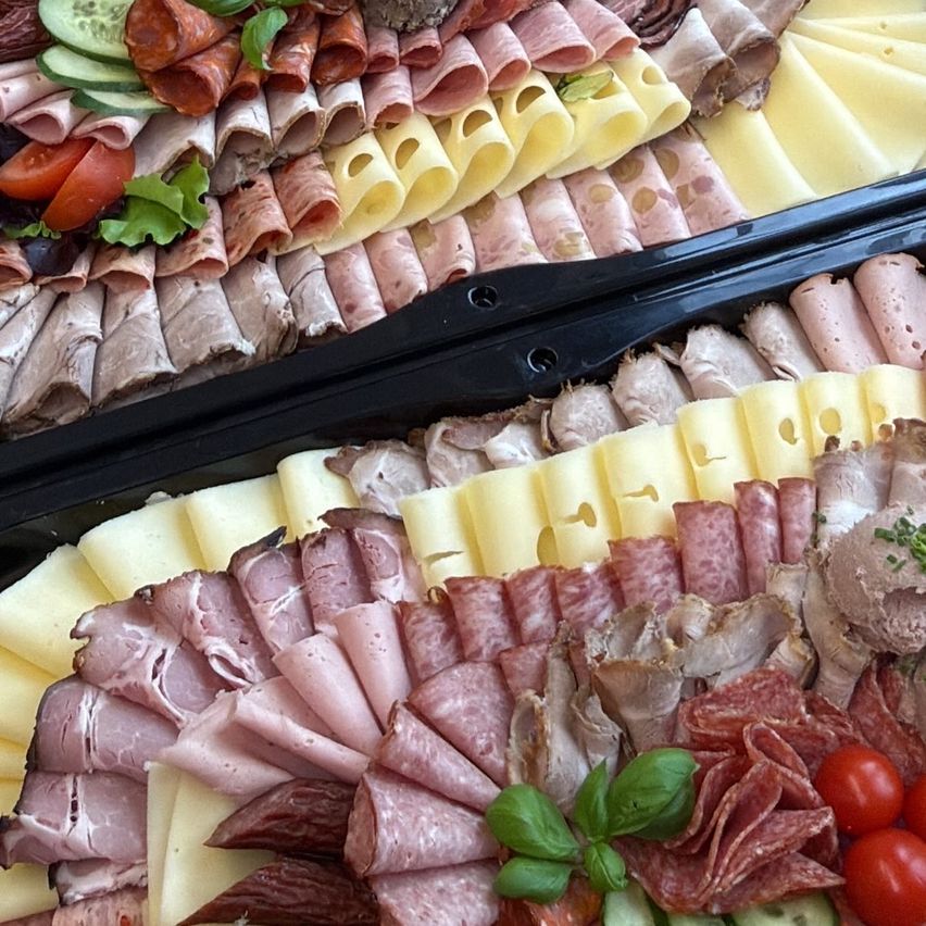 A buffet of assorted meats, cheeses, and vegetables is arranged in two trays. Various types of sliced meats, cheese, and vegetables are displayed.