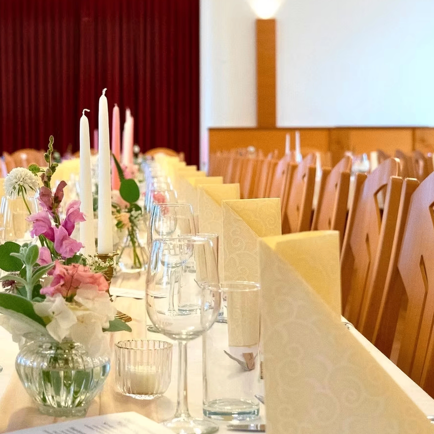 Ein Tisch für eine formelle Veranstaltung mit Blumen, Kerzen und Gläsern auf einem Tisch mit Stühlen und Vorhängen im Hintergrund.