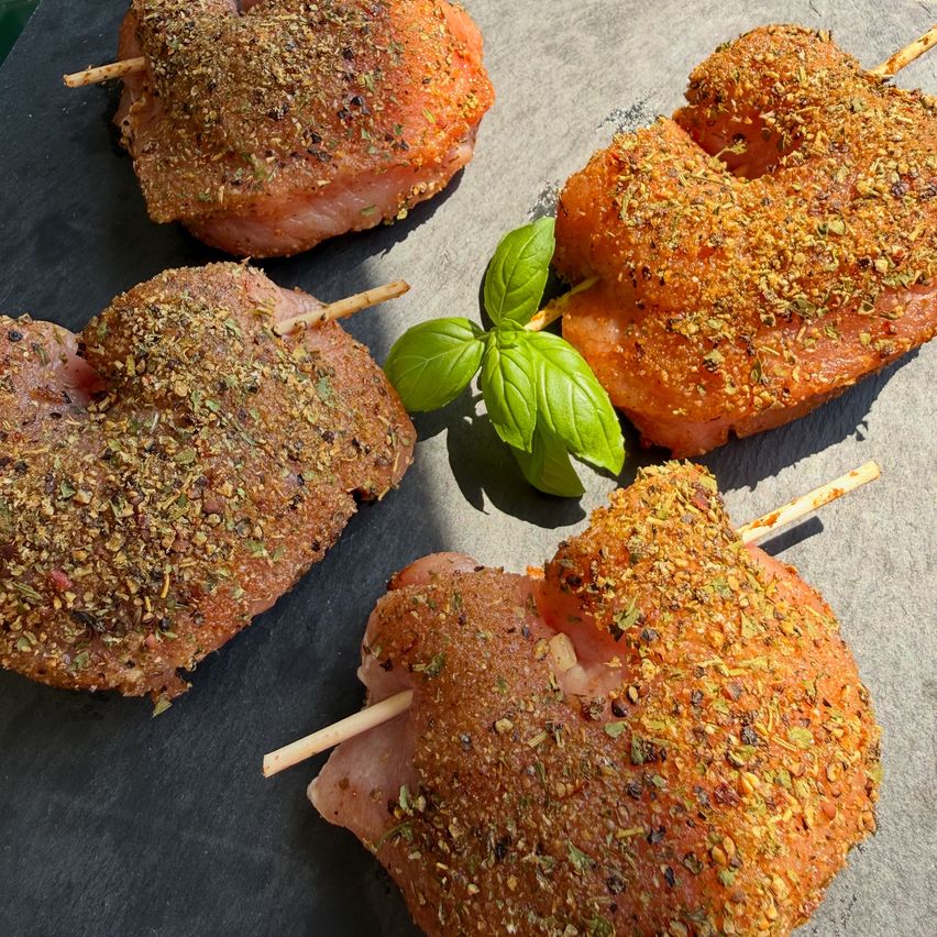 Five pieces of seasoned chicken on sticks with herbs on a gray surface.