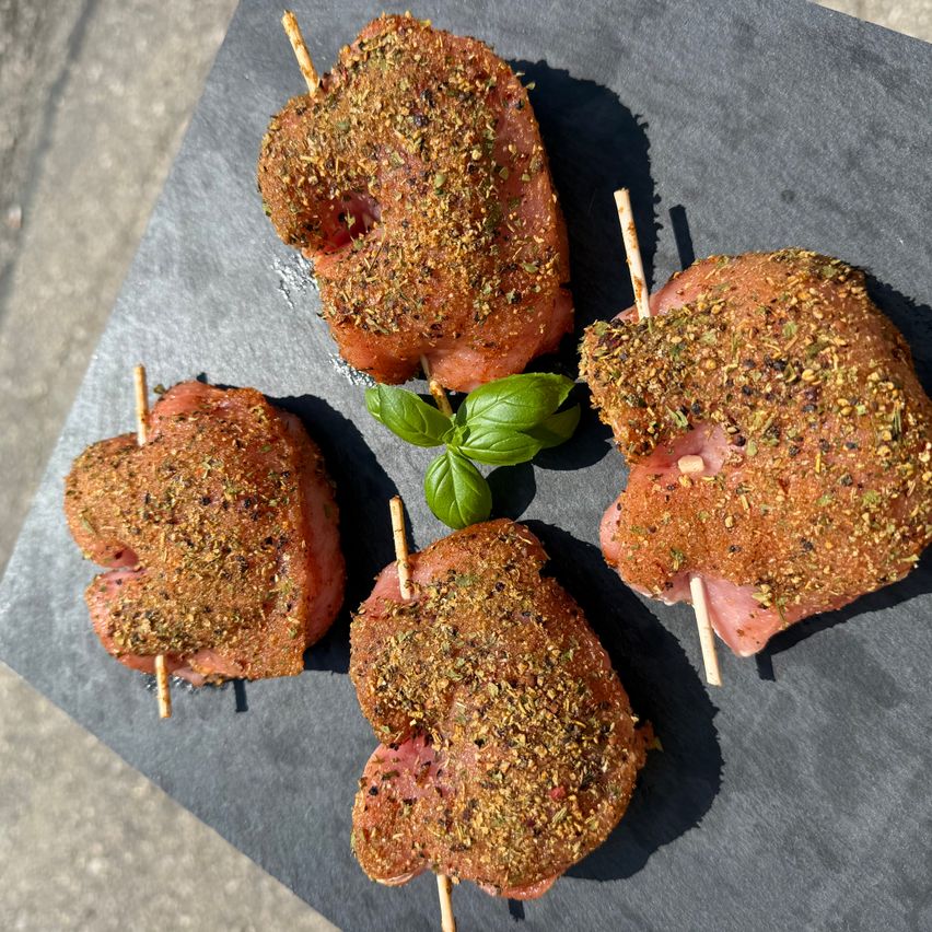 Four seasoned meat skewers with herbs on a gray surface, one with a basil leaf on top.