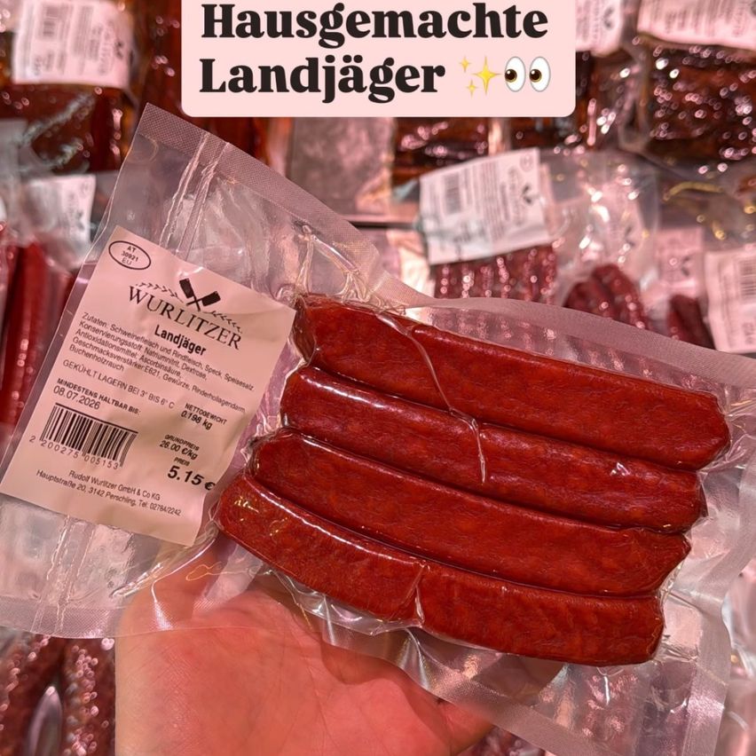 Handmade country sausages in plastic packaging, held by a hand. The text 'Hausgemachte Landjaeger' is on the top.