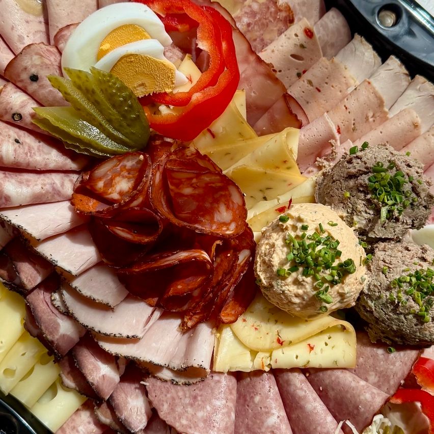 A charcuterie board features sliced meats, cheeses, hard-boiled eggs, pickles, and red peppers. Various dips are also included.