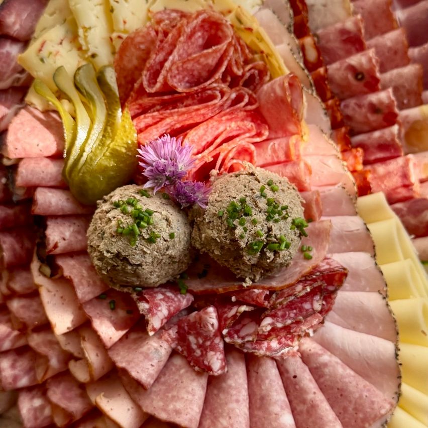 An assortment of deli meats and cheese arranged on a platter with pickles and flowers.
