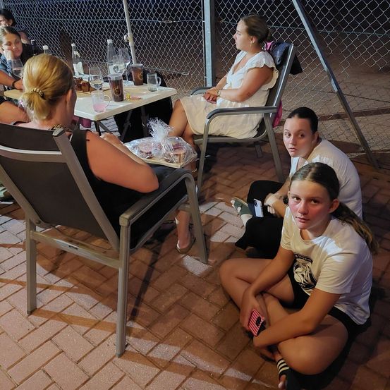 Eine Gruppe von Frauen sitzt um einen Tisch und auf dem Boden herum, möglicherweise bei einem Picknick bei Nacht.