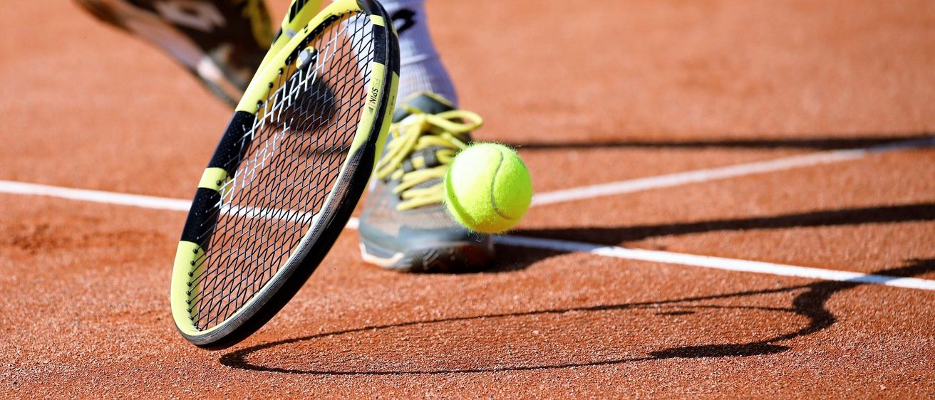 Ein Tennisspieler, der kurz davor steht, einen Tennisball mit seinem Schläger auf einem Sandplatz zu schlagen.