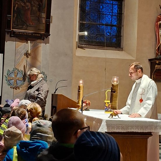 Ein Priester leitet eine religiöse Zeremonie in einer Kirche, mit einem Altar, Kerzen und einer anwesenden Gemeinde.
