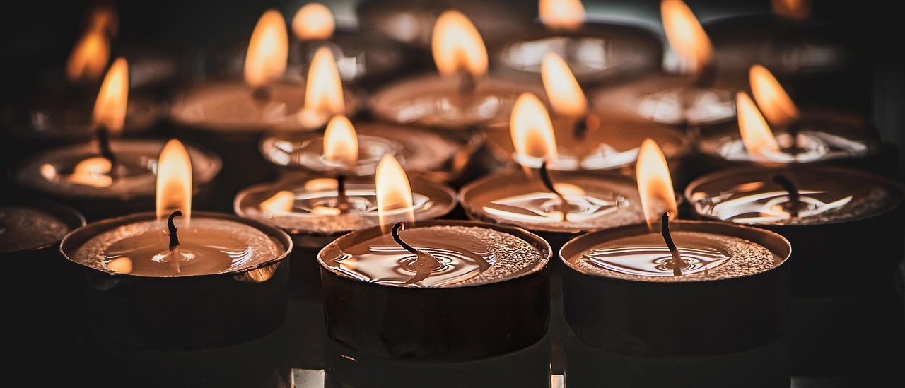 Eine Nahaufnahme von mehreren brennenden Kerzen in schwarzen Haltern, deren Flammen hell gegen einen dunklen Hintergrund brennen.