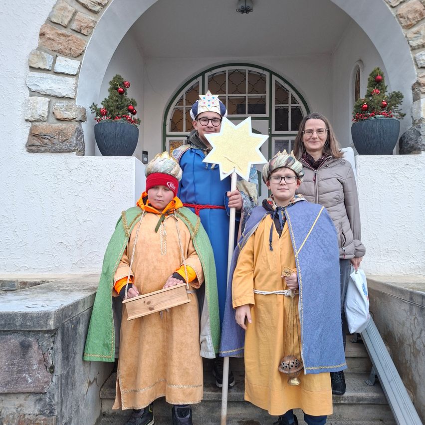 Vier Personen in mittelalterlichen Kostümen stehen auf den Stufen vor einem Gebäude. Ein Mann hält einen Stern, während eine Frau und zwei Kinder ihn begleiten.