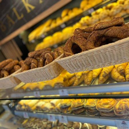 Eine Bäckerei-Auslage mit verschiedenen Gebäcksorten, darunter Croissants, Brötchen und dänisches Gebäck, auf mehreren Regalen und unter einem Schild, das 'BÄCKEREI' steht.