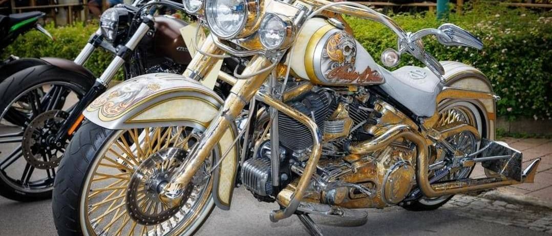 Eine goldene und weiße Motorräder mit Totenkopf-Design steht vor einem Restaurant. Menschen sitzen an Tischen hinter dem Motorrad.