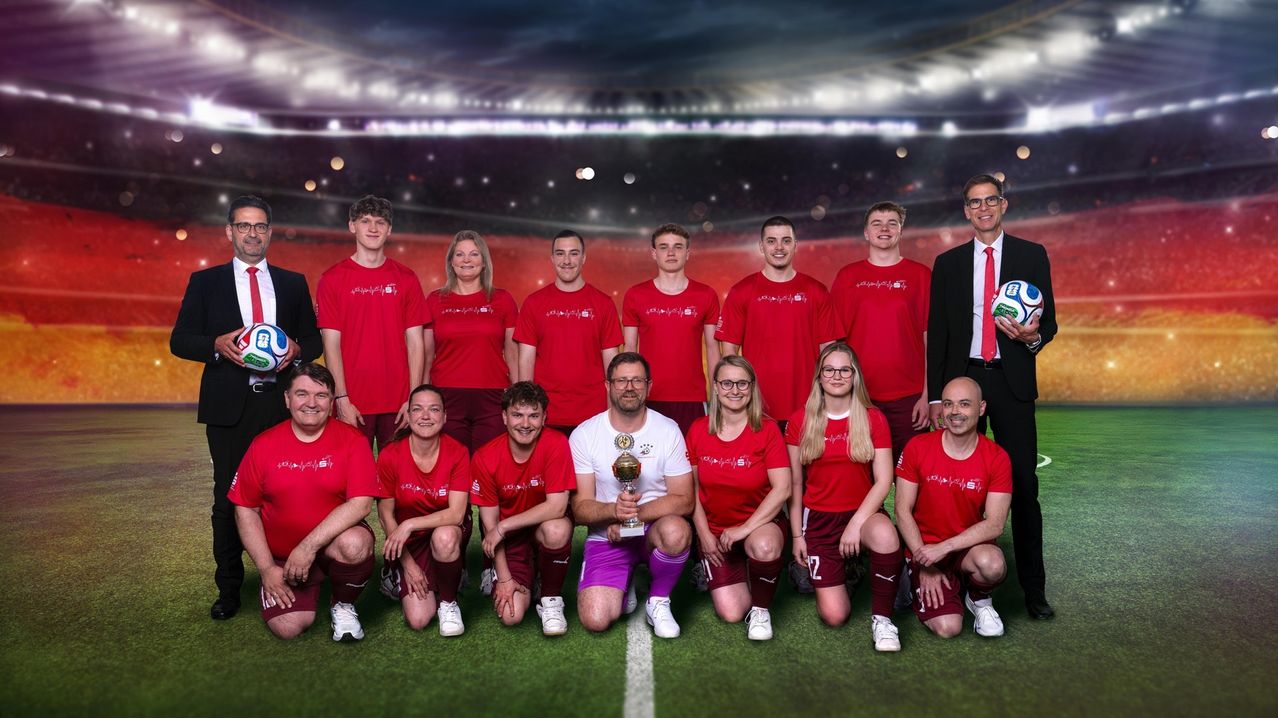 A soccer team in red jerseys poses with a trophy on a field, with a stadium background.