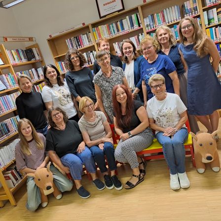 Eine Gruppe von Frauen und Mädchen posiert für ein Foto in einer Bibliothek mit Bücherregalen im Hintergrund. Einige sitzen auf einer Bank, während andere stehen.