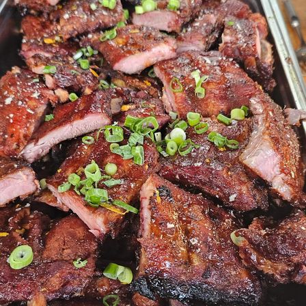 Gegrillte Rippchen in einer Schale, überzogen mit Frühlingszwiebeln und rötlicher Glasur. Einige Rippchen haben verkohlte Ränder.