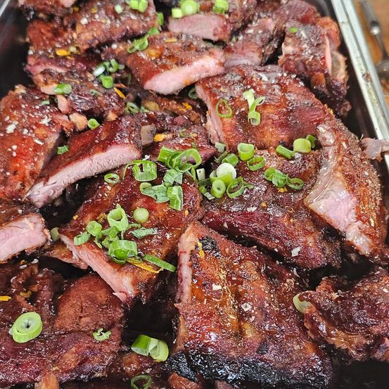 Gegrillte Rippchen in einer Schale, überzogen mit Frühlingszwiebeln und rötlicher Glasur. Einige Rippchen haben verkohlte Ränder.