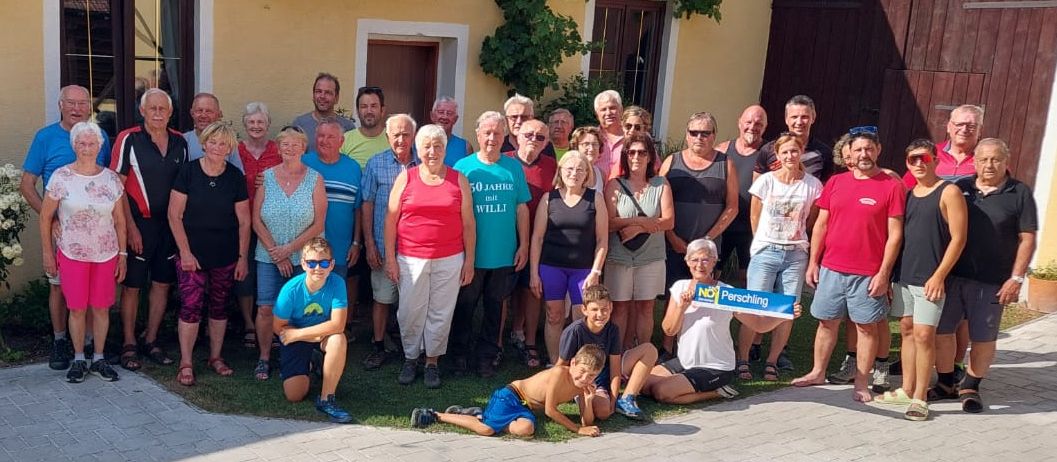 Eine Gruppe von Menschen, darunter Männer und Frauen, posiert für ein Foto vor einem gelben Gebäude mit einem Schild, das 50 Jahre mit Will liest.