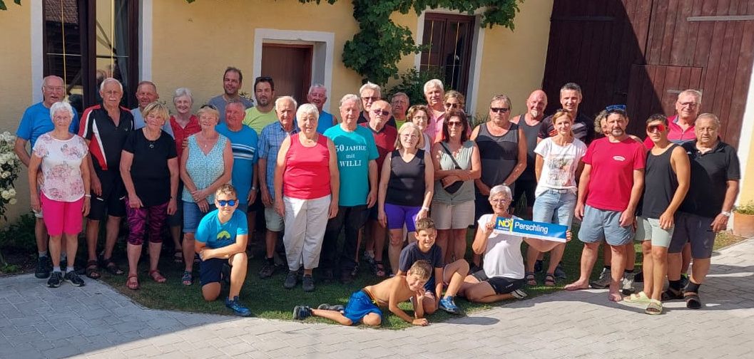 Eine Gruppe von Menschen, darunter Männer und Frauen, posiert für ein Foto vor einem gelben Gebäude mit einem Schild, das 50 Jahre mit Will liest.