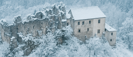 Ein Poster bewirbt eine Veranstaltung auf Burg Reichenstein am 8. Dezember 2025 um 9:00 Uhr mit einem schneebedeckten Haus, umgeben von Bäumen und einem Berg im Hintergrund.