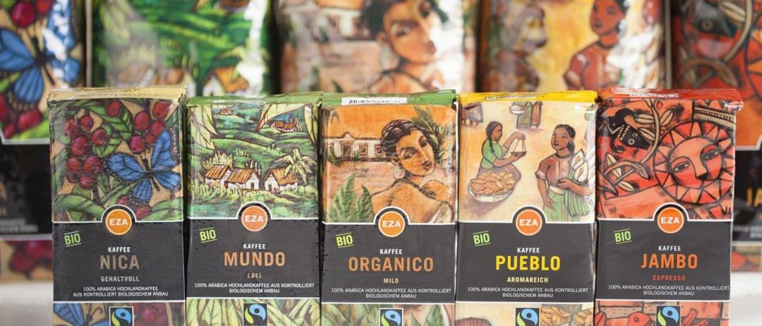 Mehrere Schachteln Bio-Kaffee sind aufgereiht mit Illustrationen von Menschen und Landschaften. Die Schachteln sind als Mundo, Organico und Pueblo gekennzeichnet. Sie sind Teil eines Fairtrade-zertifizierten Produkts.