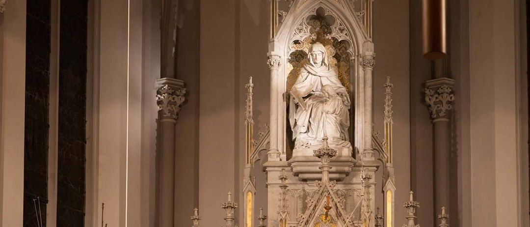 Eine weiße Statue einer Frau mit einem Baby auf dem Schoß sitzt auf einem verzierten Altar in einer Kirche.