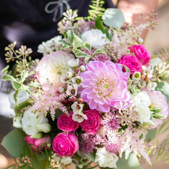 Ein Nahaufnahme eines Hochzeitsstraußes mit rosa und weißen Blumen, einschließlich Rosen, Dahlien und Grünpflanzen.