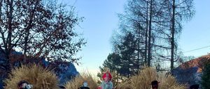 Eine Gruppe von Menschen in Kostümen, einschließlich des Weihnachtsmanns, läuft auf einem Pfad in einem ländlichen Gebiet. Sie tragen Bündel Stroh.