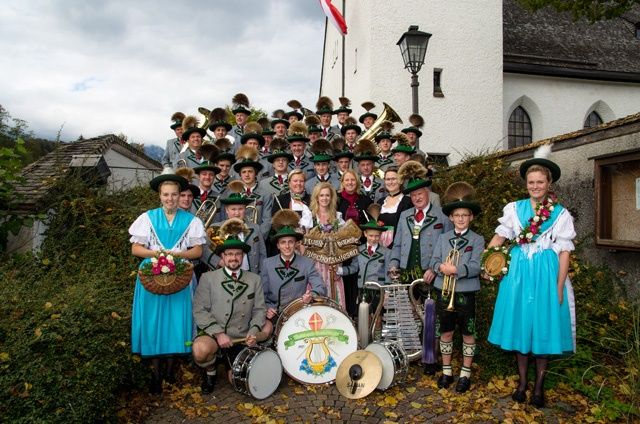 A group of people dressed in traditional attire, holding musical instruments, pose for a photo in front of a church.